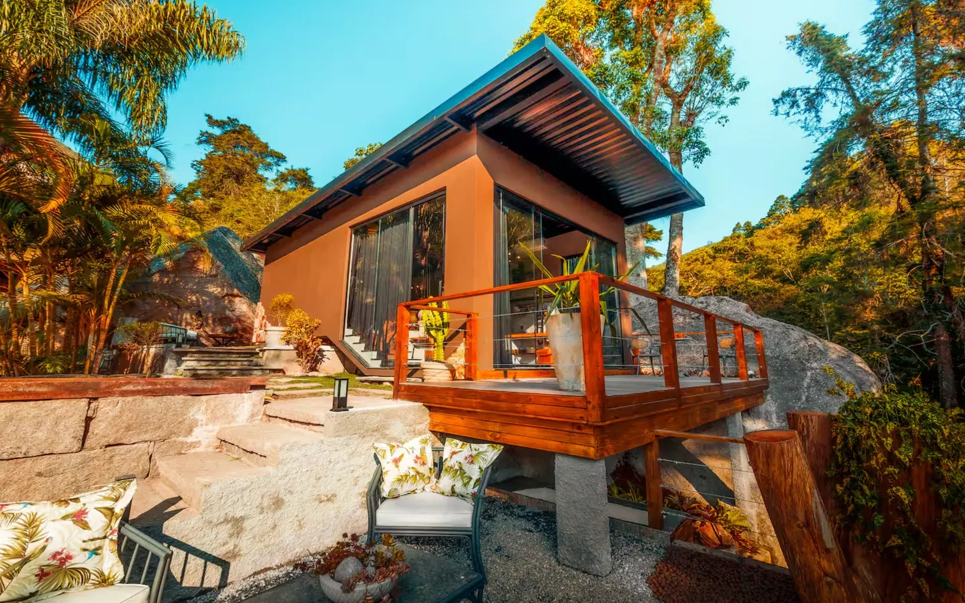 Cabana de madeira e vidro sobre a pedra, cercada pela mata da serra de Petrópolis